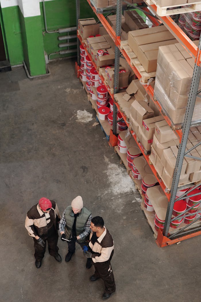 Group of warehouse workers discussing logistics and inventory in a large storage area with shelves and packages.